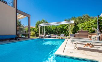 a beautiful backyard with a swimming pool , sun loungers , and umbrellas under a clear blue sky at Tina