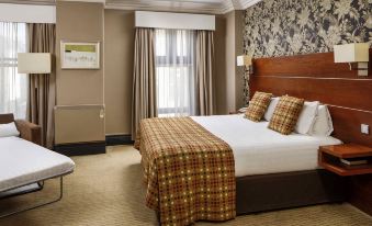 a large bed with a wooden headboard and plaid comforter is in the middle of a room at Mercure Bradford Bankfield Hotel