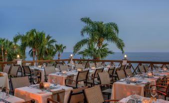 an outdoor dining area at a restaurant overlooking the ocean , with tables and chairs set for guests at Mediterranean Beach Hotel