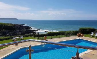 a large swimming pool surrounded by a patio , with a view of the ocean in the background at Watersmeet Hotel