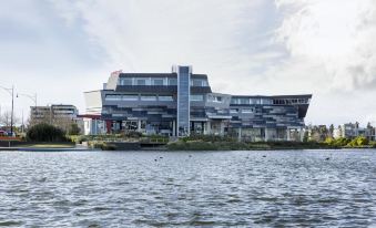 a large building is situated on the side of a body of water , with a boat passing by in front of it at Mercure Melbourne Caroline Springs