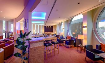 a large , well - lit room with multiple tables and chairs arranged for a gathering or event at Novotel Freiburg am Konzerthaus