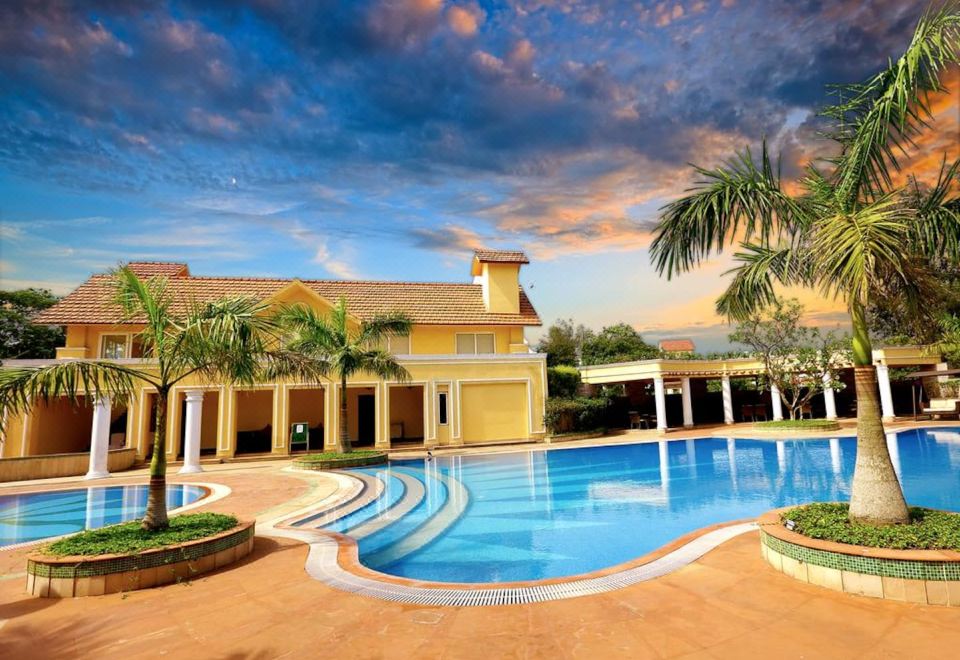 a large swimming pool with a yellow building in the background and palm trees surrounding it at Country Roads