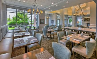 a modern restaurant with large windows , wooden tables , and chairs , and a menu displayed on the tables at Hilton Garden Inn Kent Island