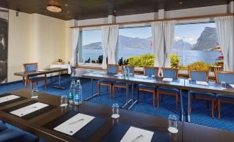a conference room with blue chairs and tables , water bottles , and a large window overlooking the water at Seehotel Kastanienbaum