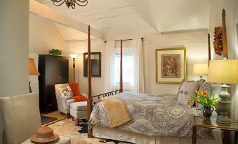 a cozy bedroom with a white bed , a chair , and a tv . the room has hardwood floors and white walls at The Inn & Tavern at Meander