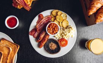 a plate of breakfast food , including bacon , sausage , beans , and potatoes , is displayed on a table at Village Hotel Farnborough