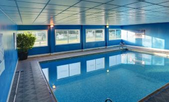 an indoor swimming pool with a blue tiled floor and walls , surrounded by windows that allow natural light to enter at Best Western Plus Centurion Hotel