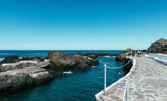 a scenic view of a rocky coastline with people walking on a path , under a clear blue sky at Hotel San Roque