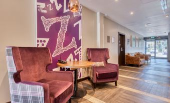a living room with two chairs , a coffee table , and a large purple wall mural at Premier Inn Bangor (Northern Ireland)