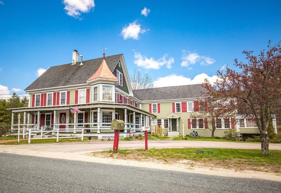 a large , two - story house with a red roof and white trim , situated on a street corner at Rosewood Country Inn