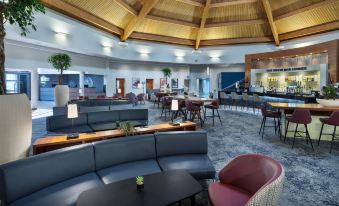 a modern lounge area with wooden ceiling , blue furniture , and large windows , including a red chair and black tables at Delta Hotels Waltham Abbey