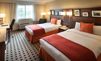 a hotel room with two beds , each made with red and white bedding , flanked by nightstands and lamps at Penn Harris Hotel Harrisburg, Trademark by Wyndham