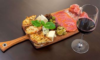 a wooden tray with a variety of food items , including salami , cheese , olives , and bread , is placed next to a glass of red at Cambria Hotel Detroit-Shelby Township