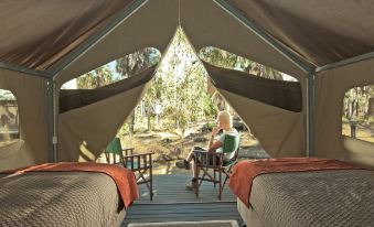 a person is sitting on a chair inside a tent with two beds and a table at Mitchell Falls Wilderness Lodge