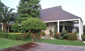 a large , two - story house with a sloping roof and brown roof tiles , surrounded by lush green trees and a wet lawn at Triple Resort