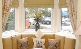 a cozy corner with a round table and cushions , next to a window with white curtains at Woodlands Hotel