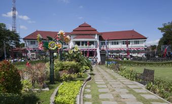a large building with a red roof and white walls is surrounded by a garden at Adel Guest House