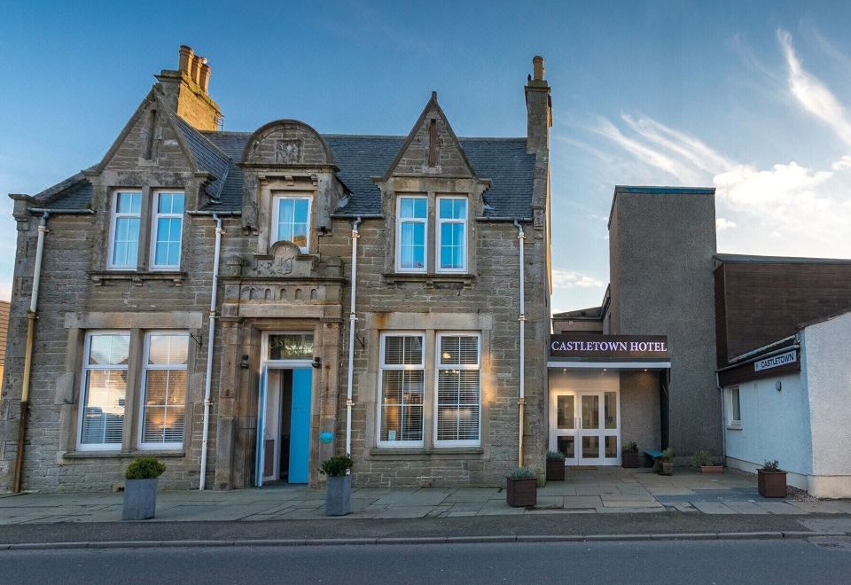 a brick building with a blue door and windows , situated in front of a street at Castletown Hotel