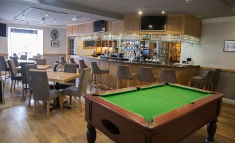a pool table is in the foreground of a room with chairs and tables , and a bar is visible in the background at The Inn at Brough