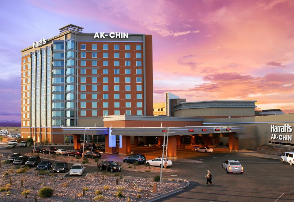 a large hotel with a pink and blue sky in the background , surrounded by cars at Harrah's Ak-Chin Casino Resort