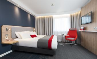 a modern hotel room with a large bed , white and gray bedding , and a red accent chair at Holiday Inn Express London - Dartford