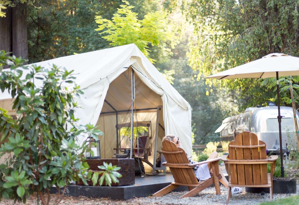 a large white tent is set up in a wooded area with two lounge chairs and an umbrella at AutoCamp Yosemite