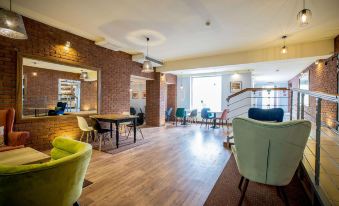 a modern office space with wooden flooring , brick walls , and various seating arrangements including green chairs and blue tables at Hotel Diament Zabrze - Gliwice