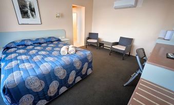 a hotel room with a blue bed , white pillows , and a chair in the corner at Copper City Motel