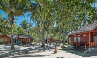 a group of small wooden cabins surrounded by palm trees on a sandy beach , with a blue sky overhead at Gangga Island Resort & Spa