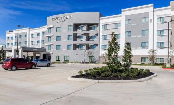 a large , modern hotel with a gray and white exterior , surrounded by trees and a parking lot at Courtyard Lake Jackson