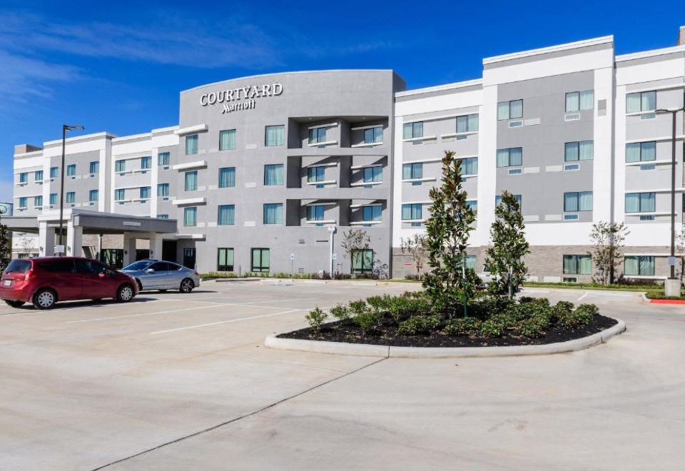 a large , modern hotel with a gray and white exterior , surrounded by trees and a parking lot at Courtyard Lake Jackson