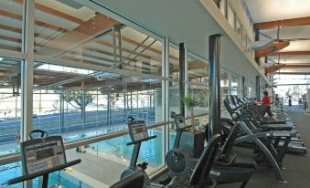 a gym with various exercise equipment , including treadmills and stationary bikes , in front of a large window at Rydges Campbelltown an EVT hotel