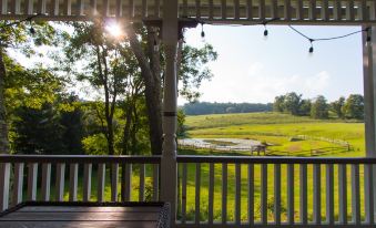 a wooden porch with a view of a green field and trees , under the setting sun at Inn at Tyler Hill