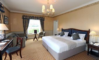 a large bed with white linens is in a room with chairs , a chandelier , and a window at Best Western Lamphey Court Hotel