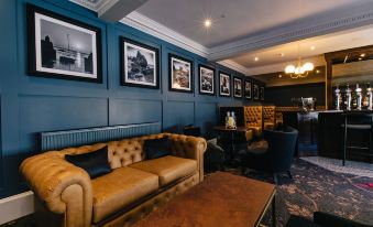 a cozy living room with blue walls , gold couches , and framed pictures on the wall at The Seafield Arms-Cullen