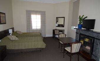 a small , empty hotel room with a bed , chairs , and a table , as well as a window at Captain Cook Hotel