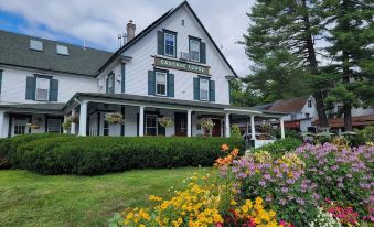 a large white house with a green roof and blue shutters , surrounded by a lush garden filled with colorful flowers at Woodstock Inn, Station and Brewery