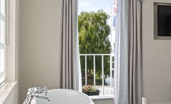 a white bathtub is placed in front of a window with a view of the outdoors , overlooking a balcony at The Mill Hotel