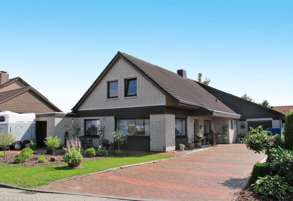 a large , two - story house with a brown roof and white walls , surrounded by lush greenery and flowers at Christine