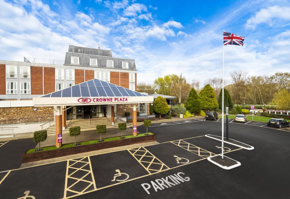 a large hotel building with a parking lot and british flag in front of it at Crowne Plaza Stratford Upon Avon