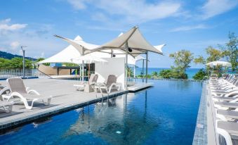 a large swimming pool surrounded by lounge chairs and umbrellas , with the ocean visible in the background at Beyond Patong