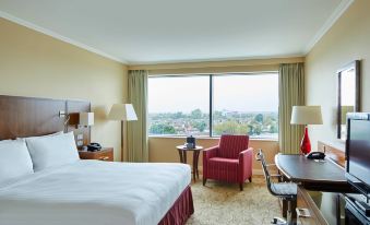 a hotel room with a large window overlooking the city , featuring a bed , desk , and chair at London Twickenham Stadium Hotel, a Member of Radisson Individuals