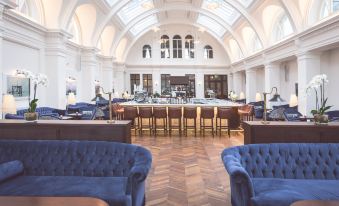 a large room with blue couches and chairs , a bar in the background , and a person standing near the counter at Titanic Hotel Belfast