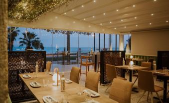 a restaurant with wooden tables and chairs , large windows offering ocean views , and white tablecloths on the tables at Hotel Meridional