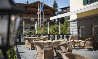 an outdoor patio with wicker chairs and a table , surrounded by flags and mountains in the background at Hotel Cristallo