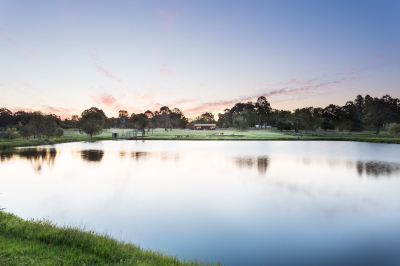 a serene landscape of a lake with trees and buildings in the background at dusk at The Swan Valley Retreat