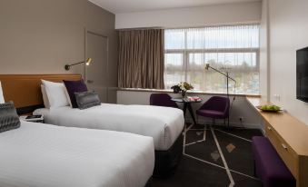 a hotel room with two beds , a window , and a chair near the window , all set against a dark carpet at Rydges Campbelltown an EVT hotel