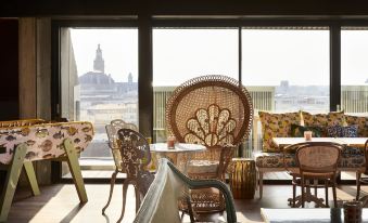 a room with a large window and colorful chairs and tables , all facing a cityscape at Mama Shelter Lille