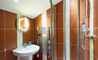 a modern bathroom with brown tiles , a sink , and a shower area , along with a towel rack and a mirror at Old Posting House